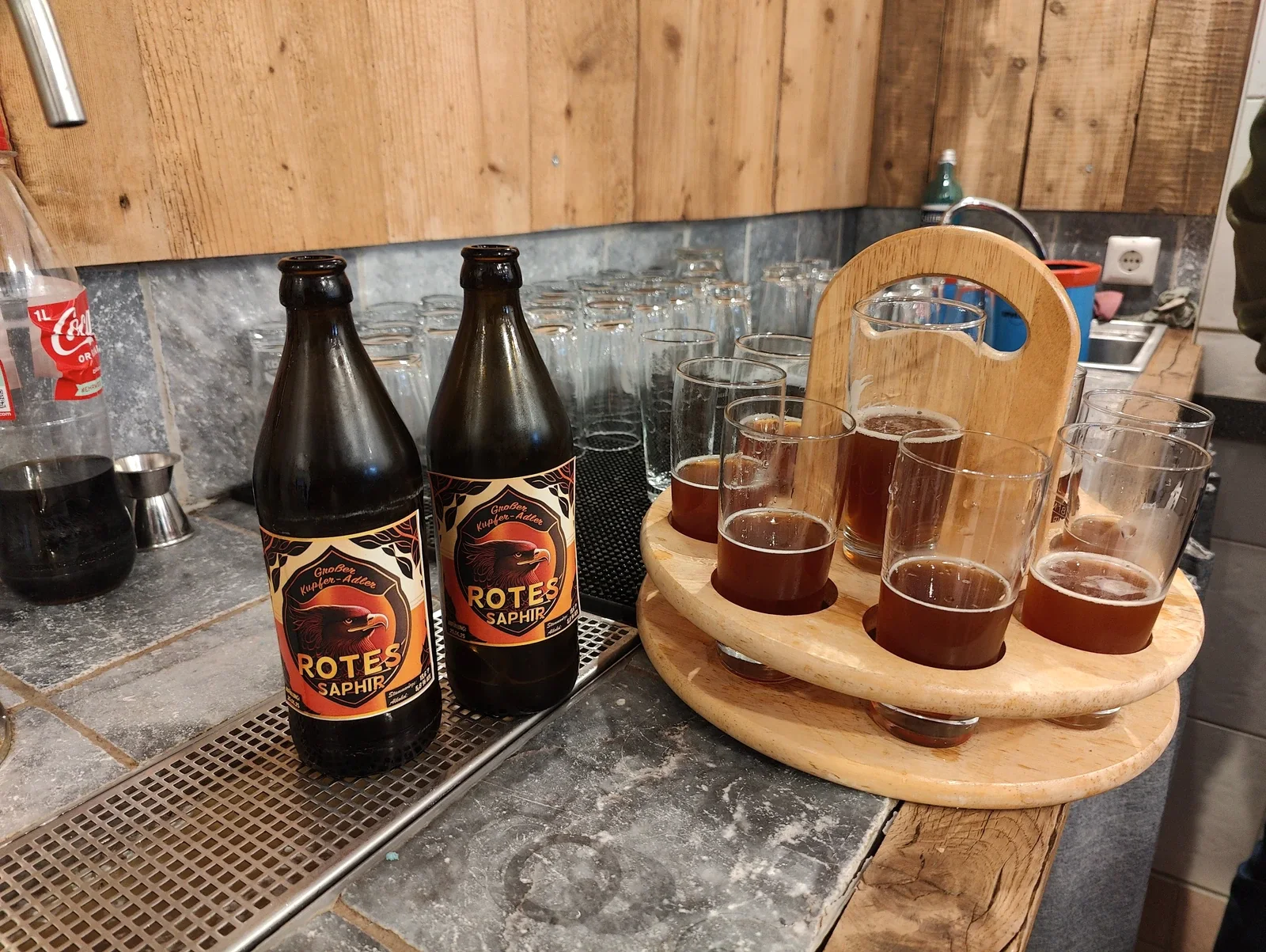 Rotes Saphir von Großer Kupfer-Adler: zwei Bierflaschen neben gefüllten Verkostungsgläsern in einem hölzernen Träger.