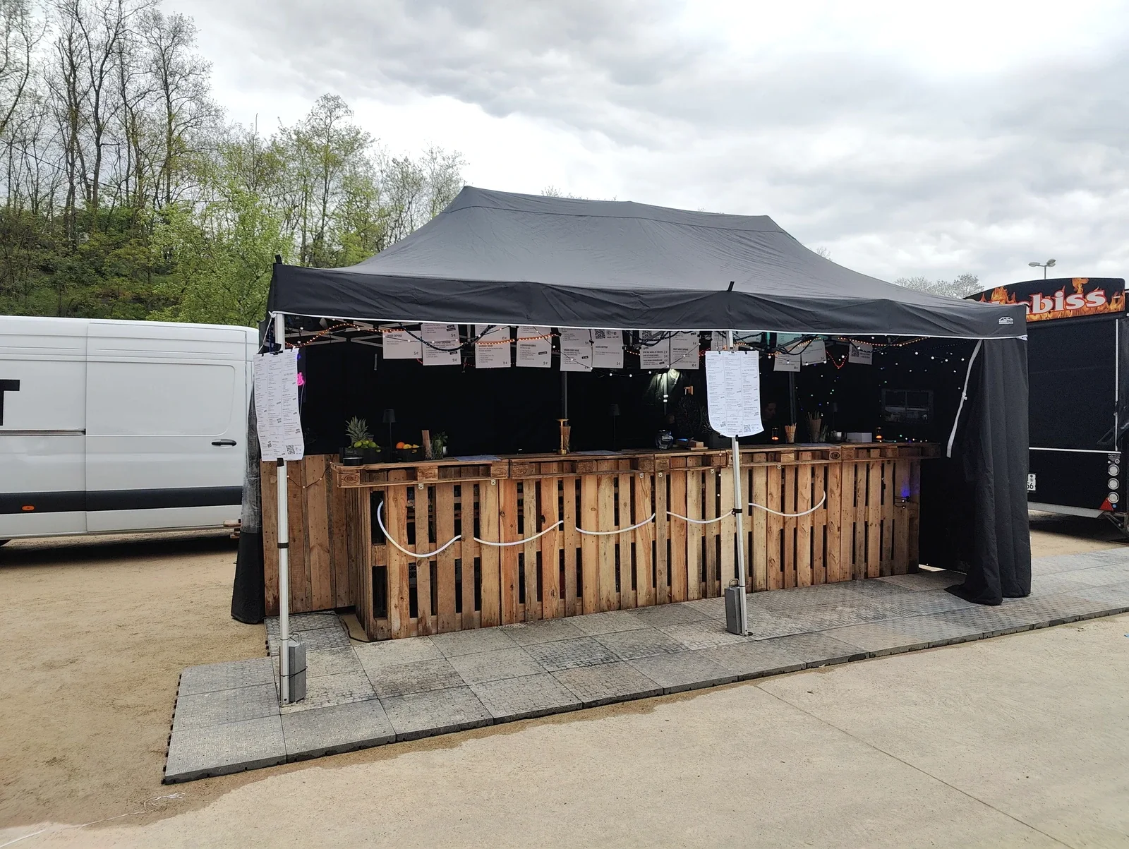 Die aufgebaute mobile Bar aus Holzpaletten mit Arbeitsfläche, Getränkekarten und schwarzer Überdachung im Einsatz.